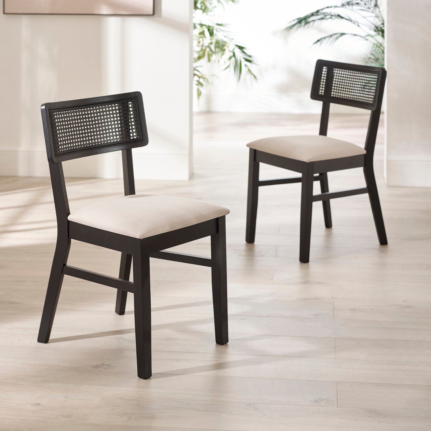 Pair of Annika black rattan back dining chairs shown together in a bright dining room setting