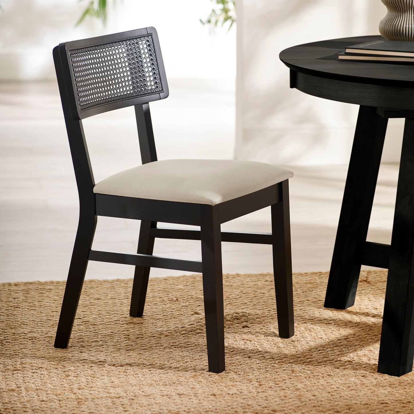 Annika black wooden dining chair with woven rattan backrest and natural fabric seat styled next to a black dining table