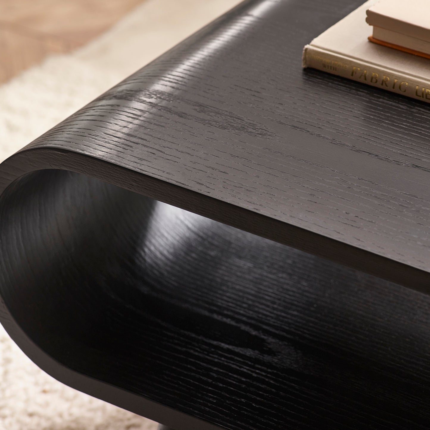 Close-up shot of the rich black ash wood grain texture and smooth curved edge on the Apollo coffee table