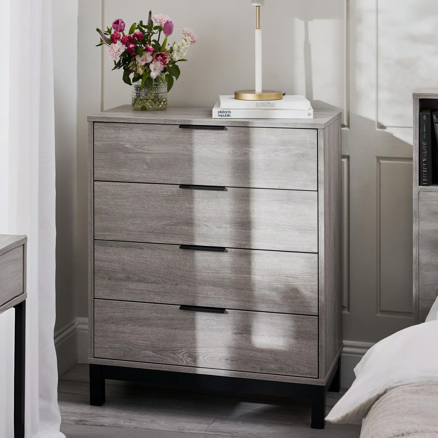 Bali grey oak effect 4 drawer chest styled in a bright modern bedroom next to flowers and books