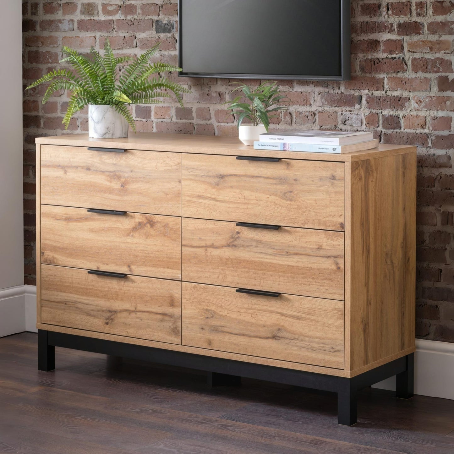 Bali natural oak effect 6 drawer wide chest styled in a brick-walled industrial bedroom beneath a TV