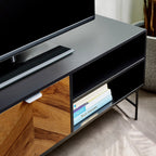 Angle view of open storage shelf compartments on a black TV unit holding books and media items.
