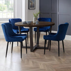 Brooklyn dark oak round dining table styled with blue velvet upholstered chairs in a dining room.