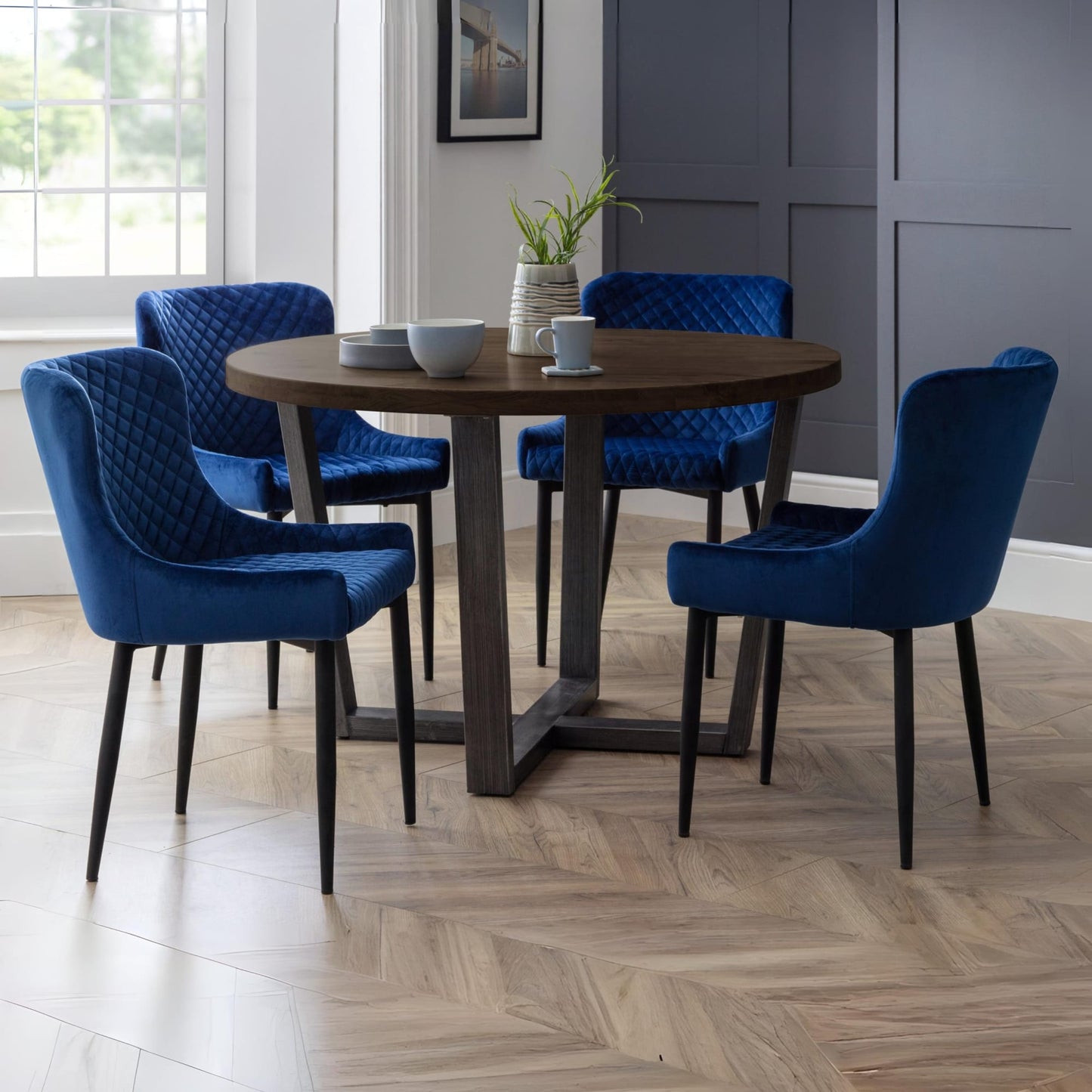 Brooklyn dark oak round dining table styled with blue velvet upholstered chairs in a dining room.