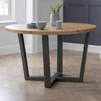 Brooklyn industrial solid oak round dining table with cross-base black metal legs in a dining room.