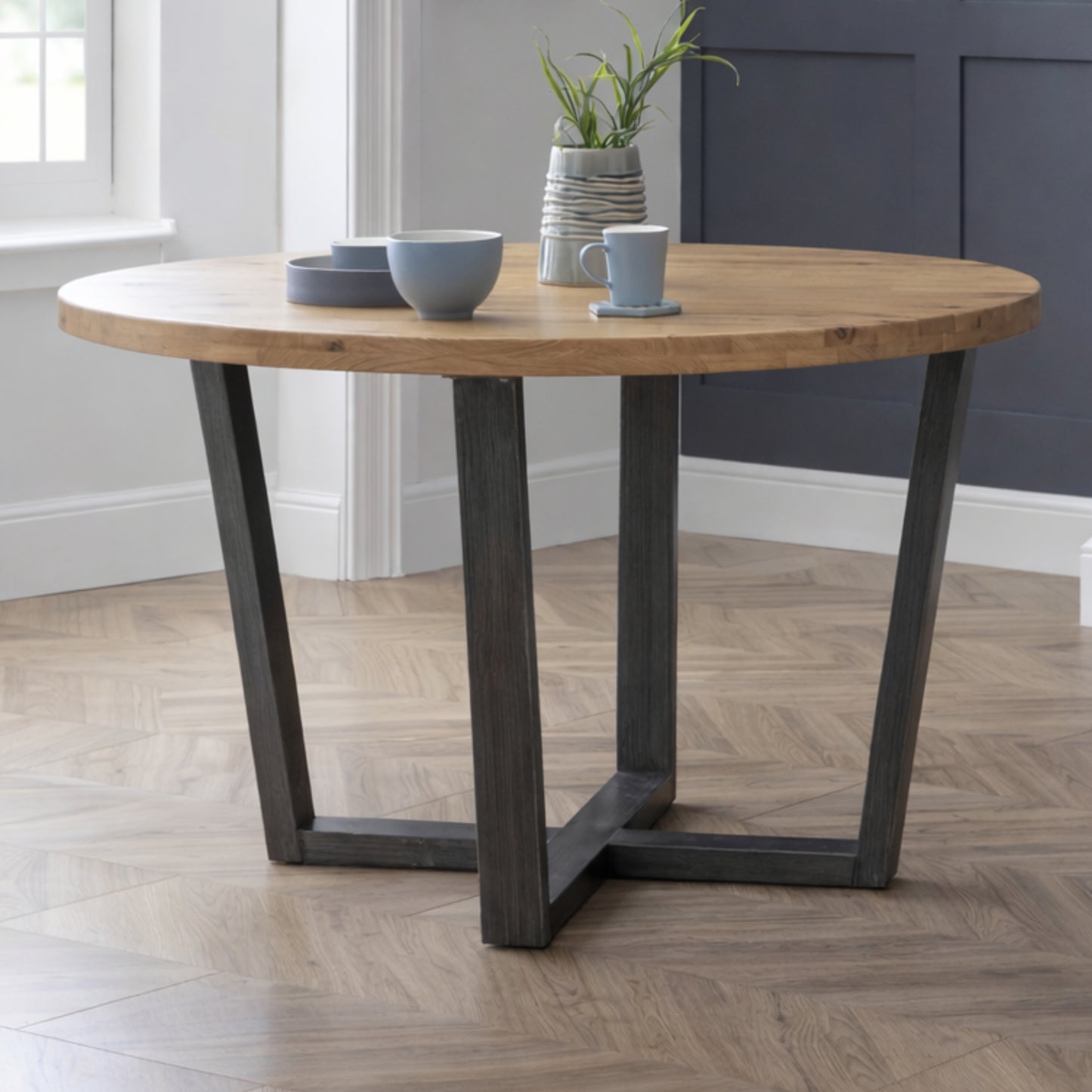 Brooklyn industrial solid oak round dining table with cross-base black metal legs in a dining room.