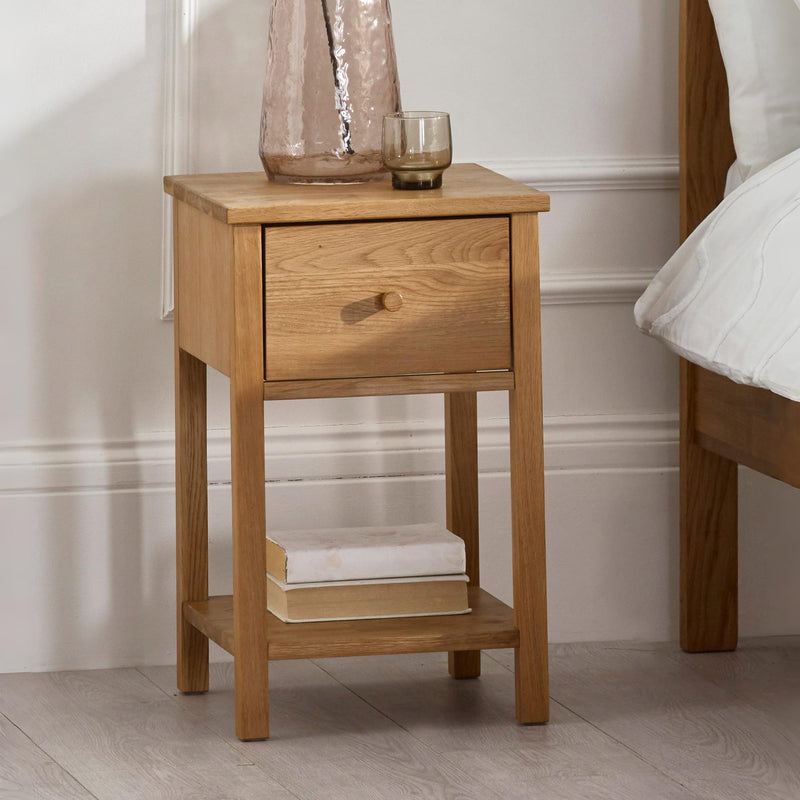Coxmoor 1 drawer solid oak bedside table styled next to a bed with decorative accessories.