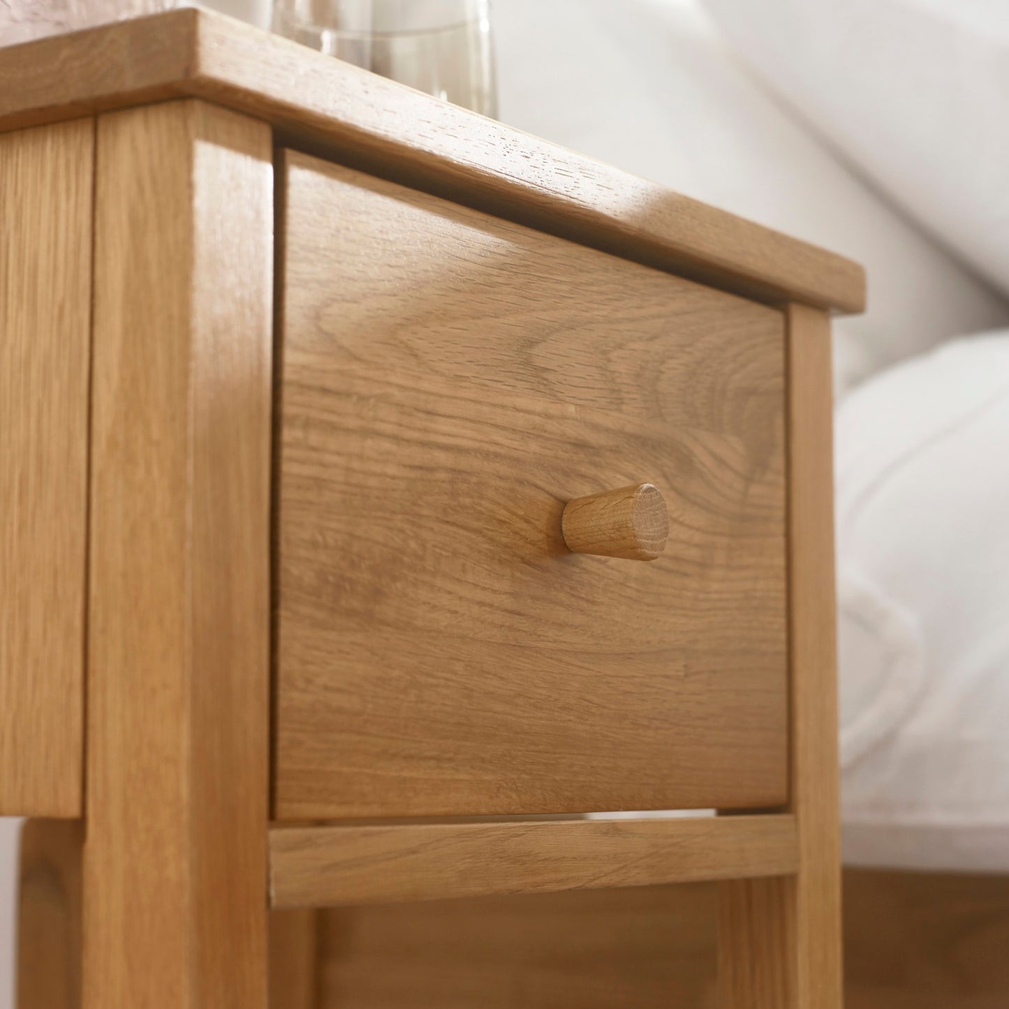 High-angle lifestyle shot of the Coxmoor oak nightstand with open drawer and lower shelf storage in a bedroom.