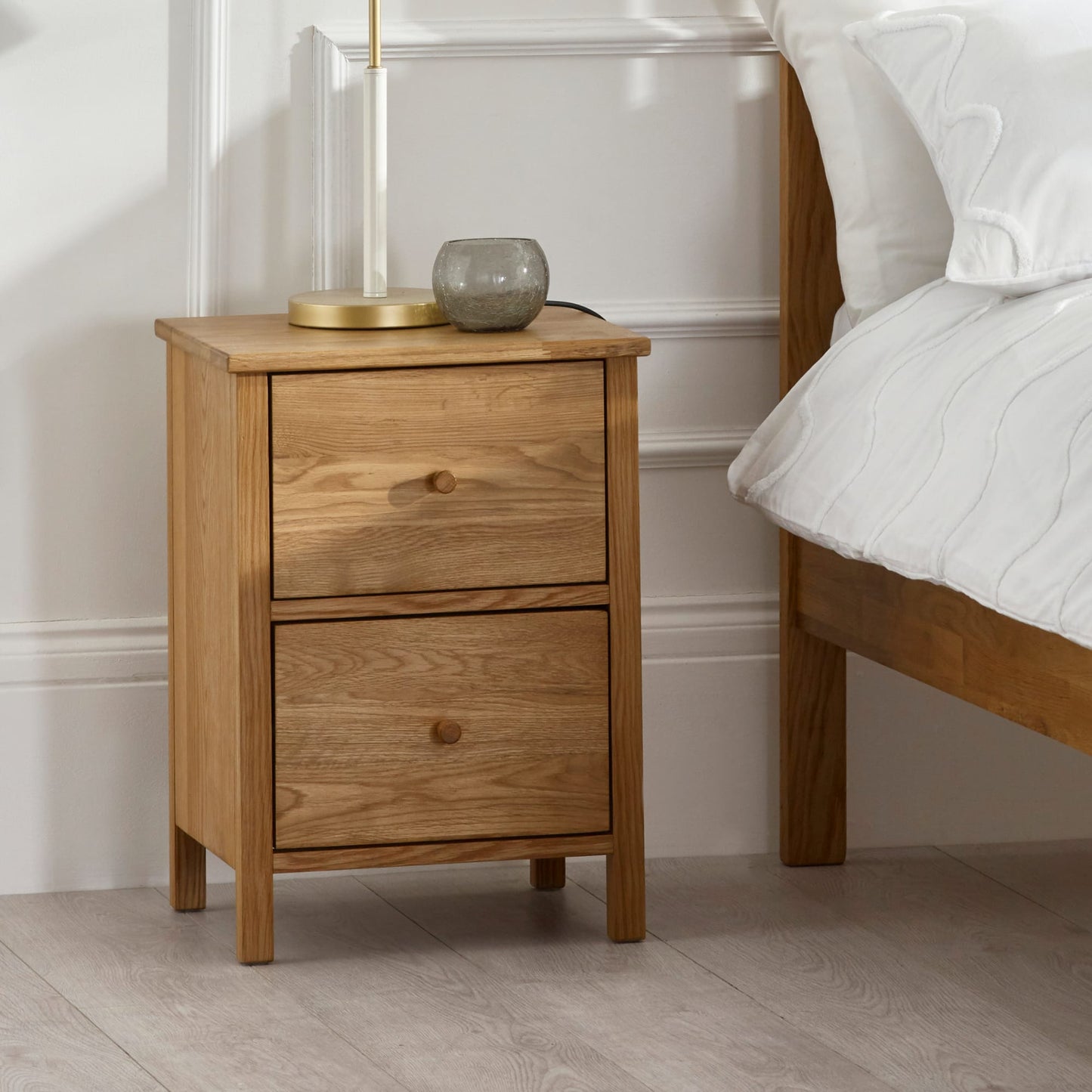 Coxmoor solid oak 2 drawer chest styled beside a bed with lamps and decorative accessories.