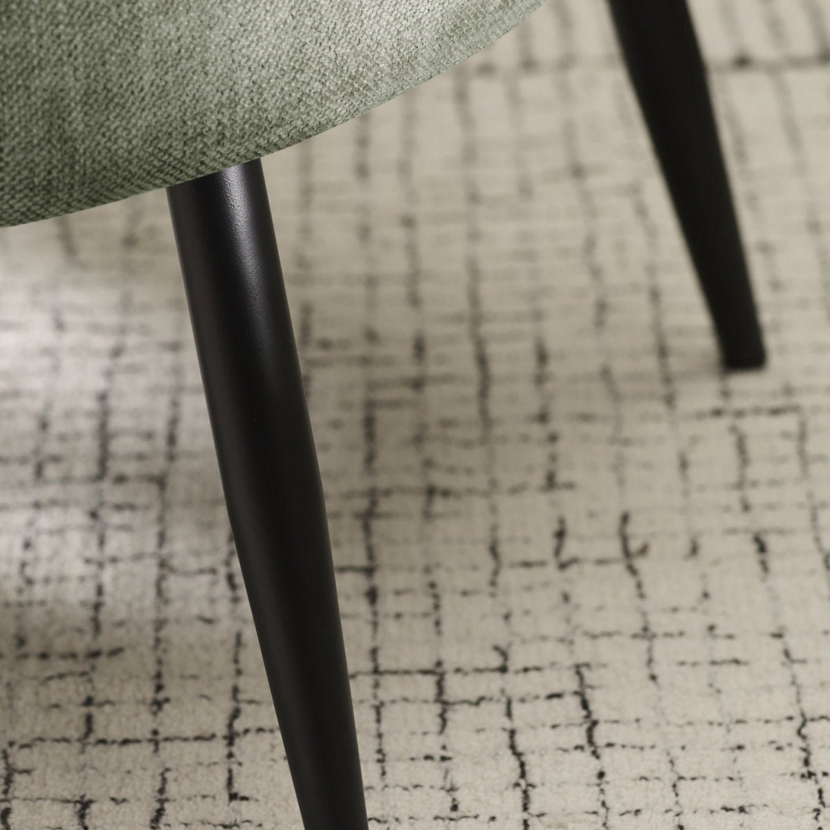Detailed shot of the sleek, tapered black powder-coated metal legs on the Dahlia accent chair