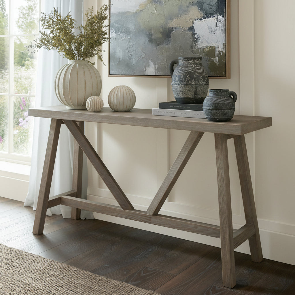 Haldon wooden trestle console table styled against a green wall with a ceramic vase, art print, and decorative jars