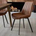 Malmo tan faux leather dining chair with channel stitching styled by a wooden dining table near a cozy fireplace