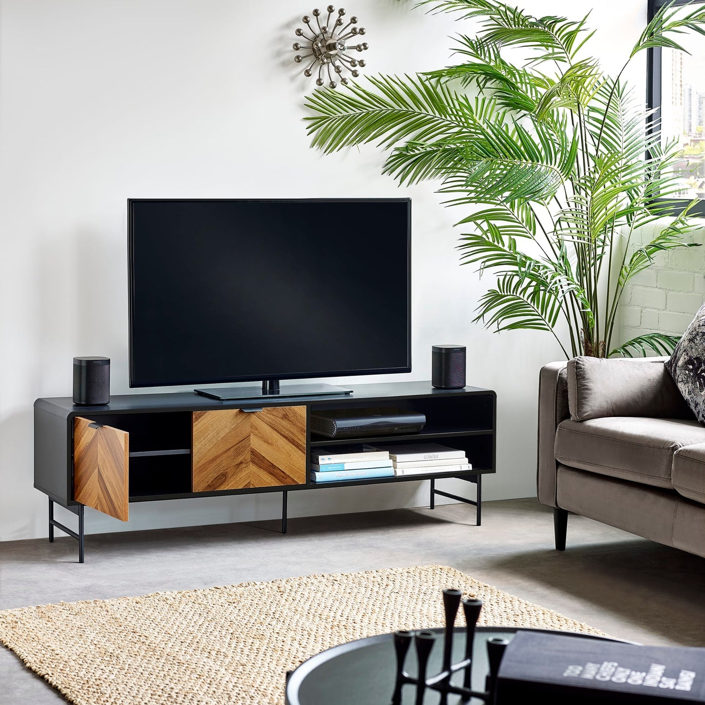 Black and wood chevron TV stand supporting a flat-screen television in a modern living room setup.