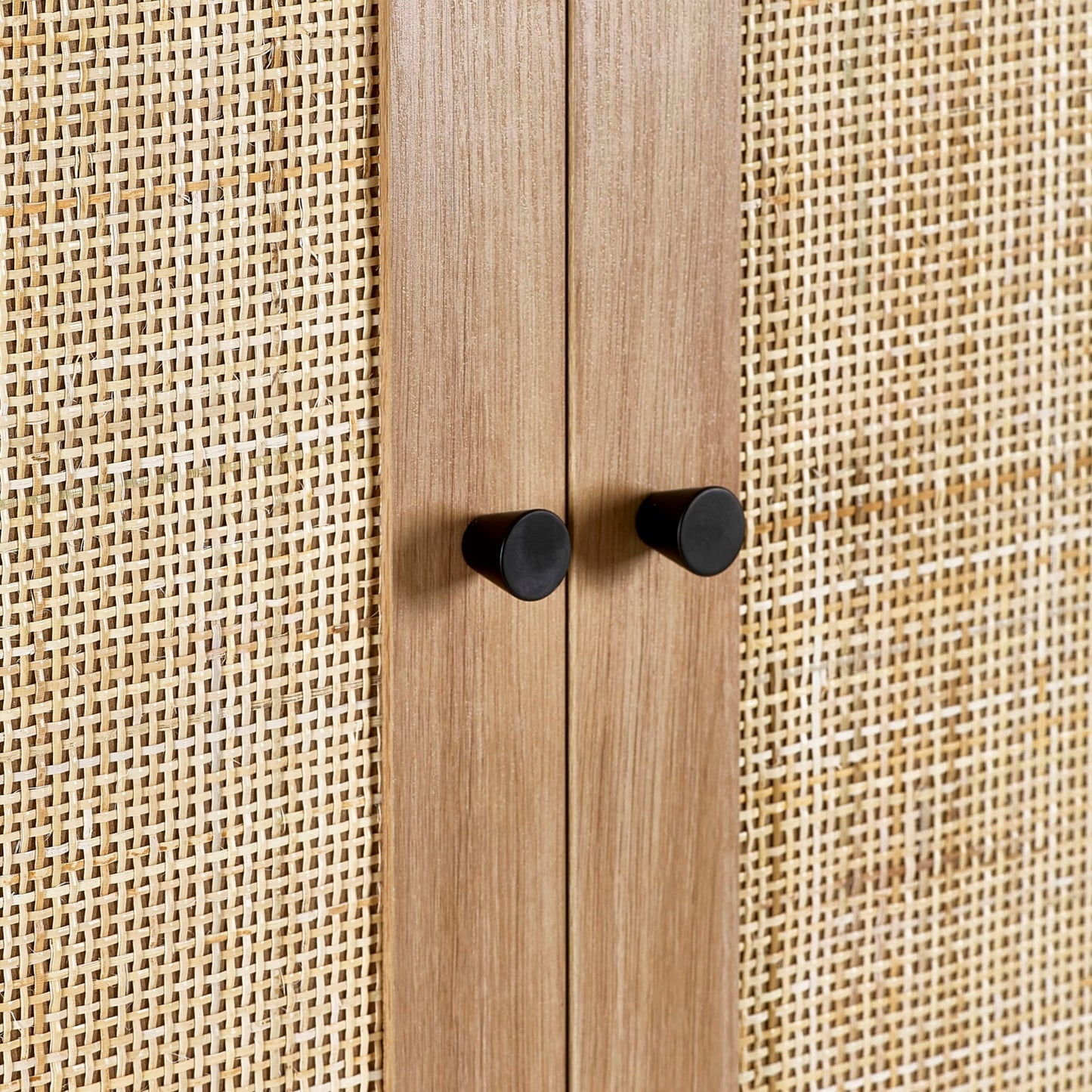 Close-up shot of the woven natural cane door panel and round black handles on the oak wardrobe