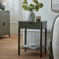 Reed fluted 1 drawer accent side table styled next to a bed with a flower vase on top and magazines on the lower shelf