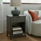 Reed fluted 1 drawer side table styled next to a lounge chair with a table lamp and books in the open cubby