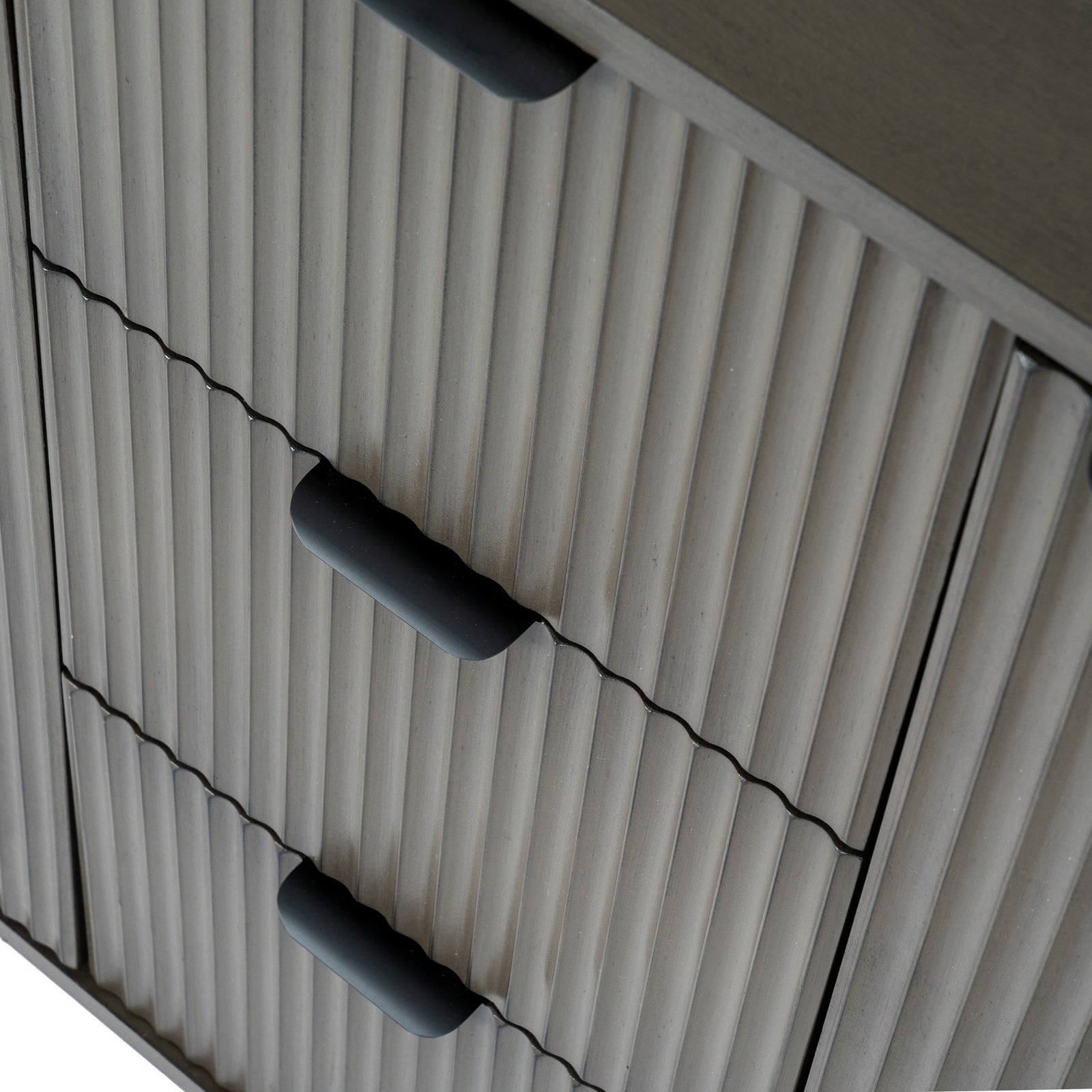 Detail view of the sleek black lip handles and fluted texture on the central drawers of the reed cabinet