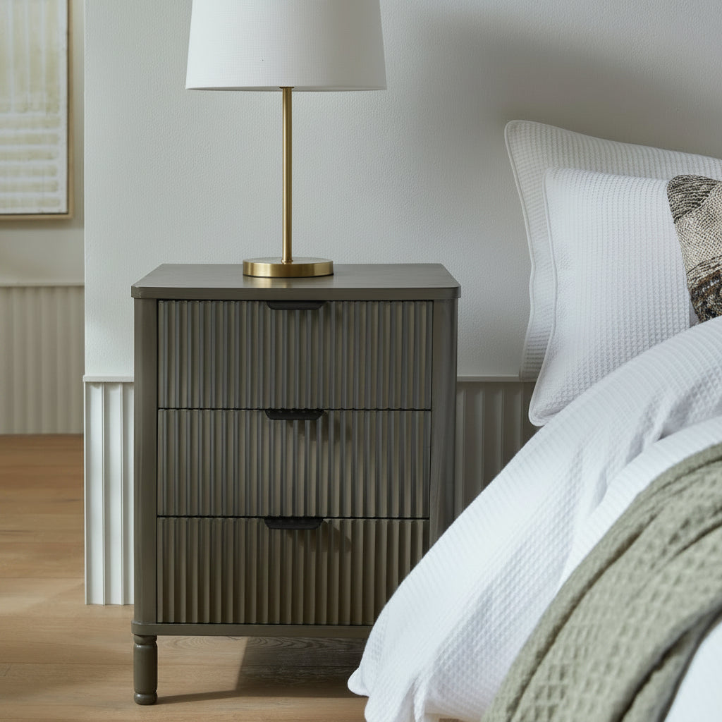 Reed fluted 3 drawer bedside table styled next to a bed with a ceramic table lamp and stacked books