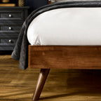 Close-up shot of the walnut-toned wood frame corner and splayed mid-century tapered leg on the Walden bed frame